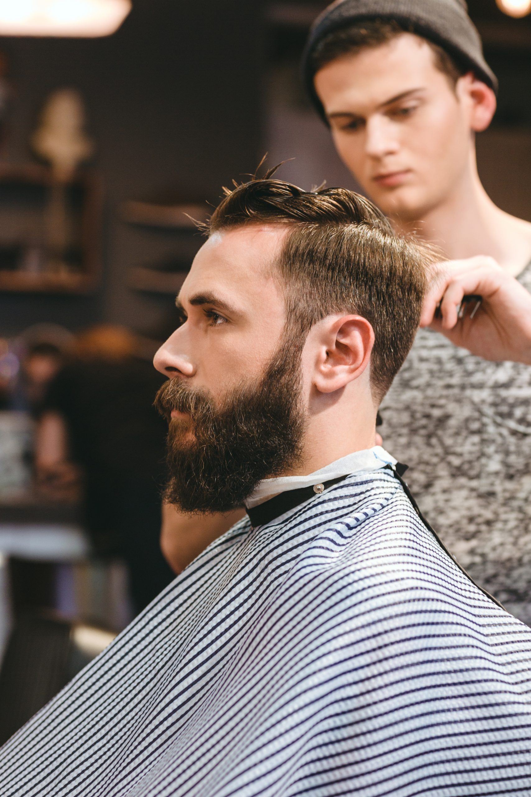 Professional hairdresser cutting young bearded man's hair in hairdressing salon